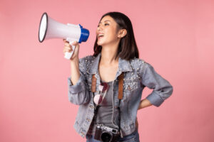 young girl talking into a megaphone sharing a message with a pink background